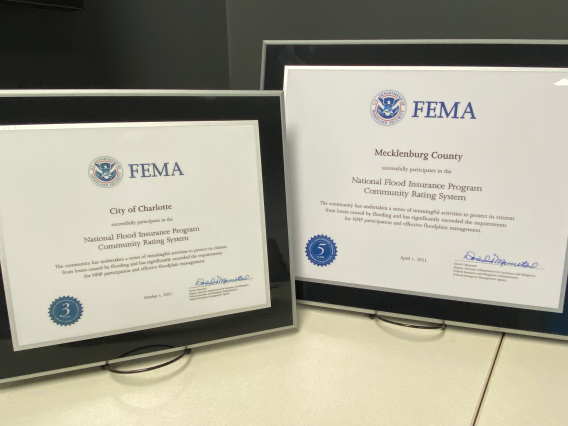 Two framed plaques for the Community Rating system. On the lleft is one for the City of Charlotte. On the right, Mecklenburg County.